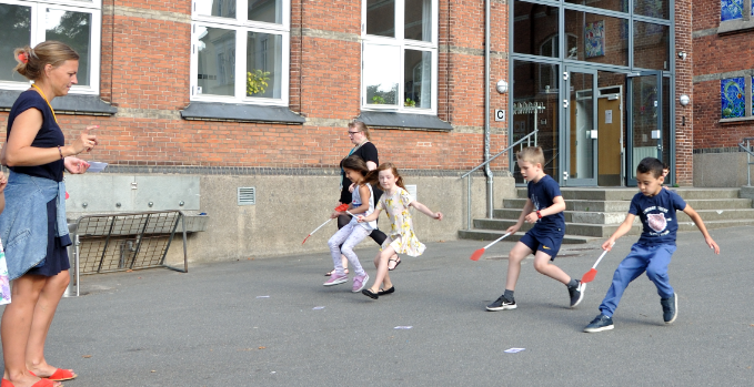 Billedet viser børn, der er i gang med et kapløb i Kildegadens skolegård, mens lærerne ser på