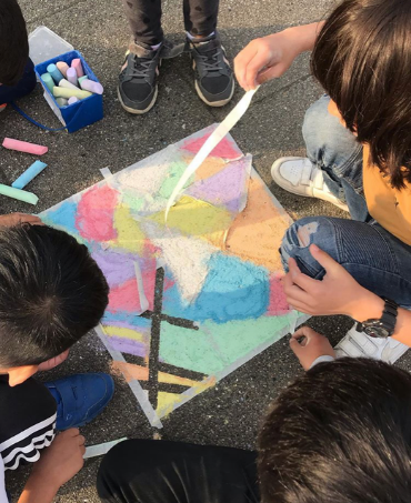 Billedet viser nogle elever, der farver et billede med farvede kridt