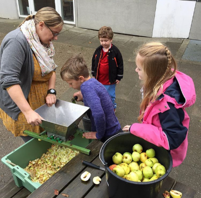 Billedet viser tre elever og en lærer, der laver æblemost i en æblepresser