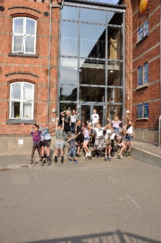 Billedet viser en gruppe skoleelever, der jubler og hopper foran indgangen på afdeling Kildegade