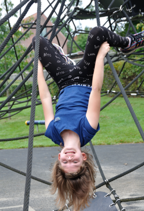 Billedet viser en glad pige, der hænger nedad på skolens klatrestativ