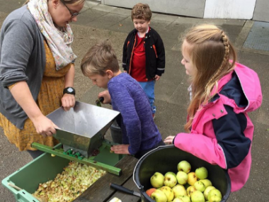 Billedet viser en lærer med tre elever, der kværner æbler, så de kan lave æblemost